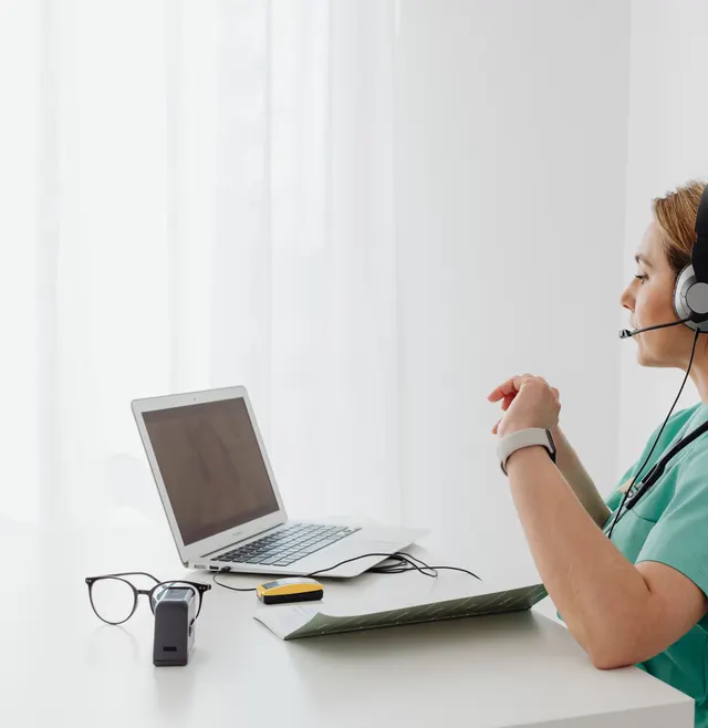 A clinician wearing a headset on a video call at her laptop